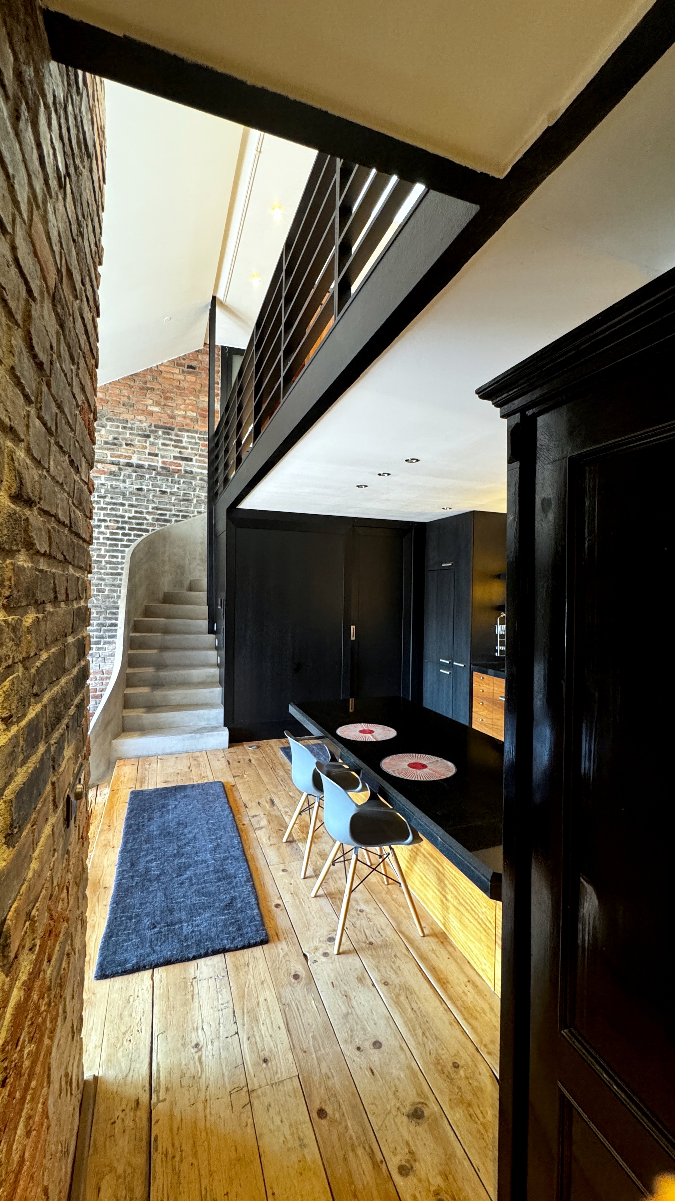 Grand entrance hall of Polska Penthouse featuring historic brick pillars, a black granite kitchen island, and a sculptural concrete spiral staircase