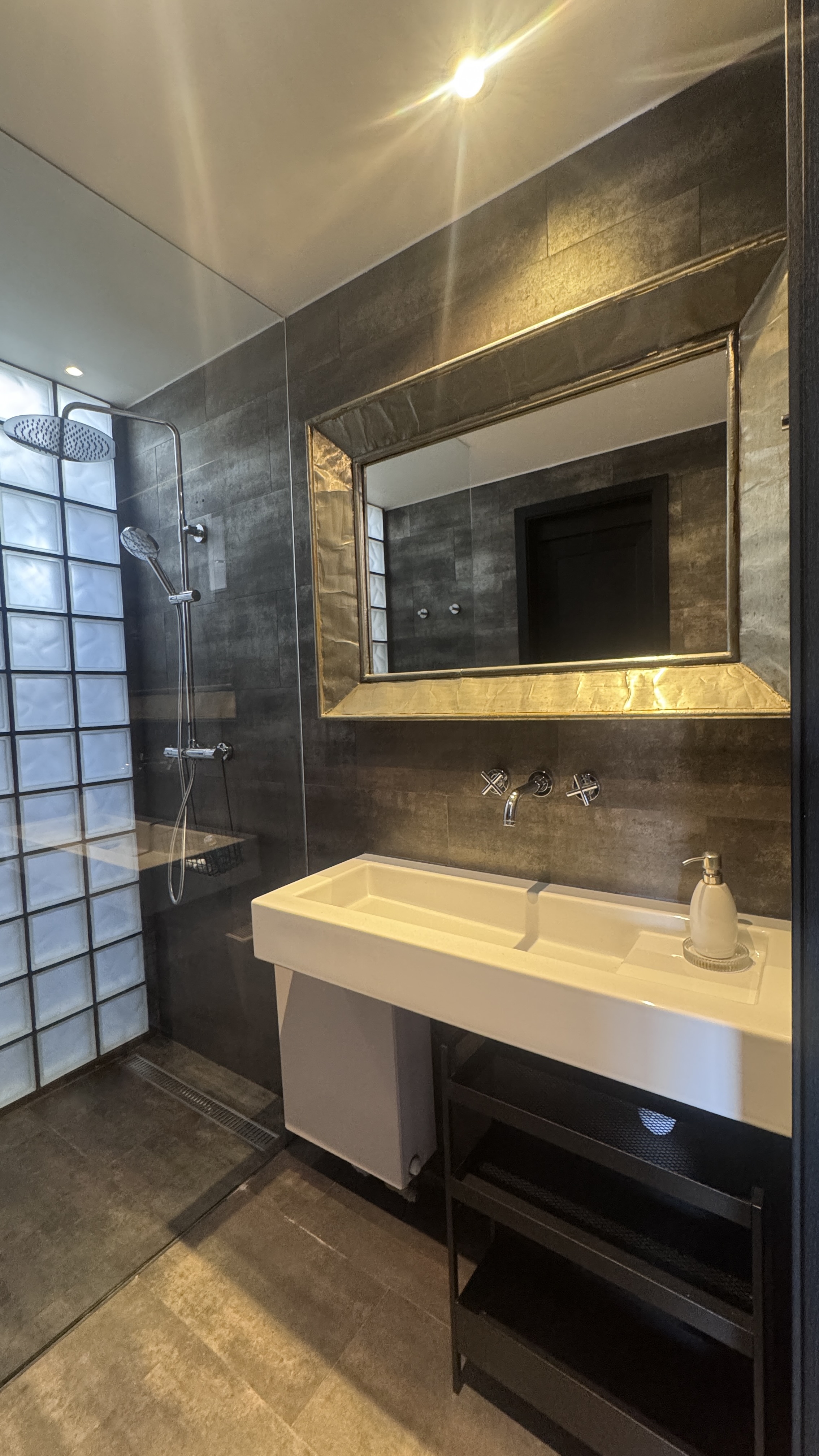 Lit shower room at Polska Penthouse — glass-block wall glowing with diffused light, mid level of the Great Room, Vinohrady